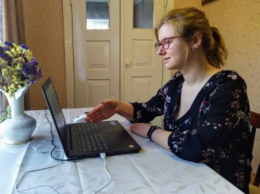 Avrupalı genç bir kadın masada oturuyor, video görüşmesi yapıyor ve evdeki dizüstü bilgisayarında el sıkışma hareketi yapıyor.