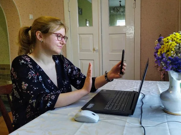 ヨーロッパの若い女性はテーブルに座り ビデオ通話をし 自宅でスマートフォンでジェスチャーを停止します — ストック写真