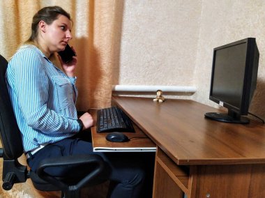 Korkak Avrupalı genç kadın masada oturur, akıllı telefonla konuşur ve evdeki bilgisayarda çalışır.