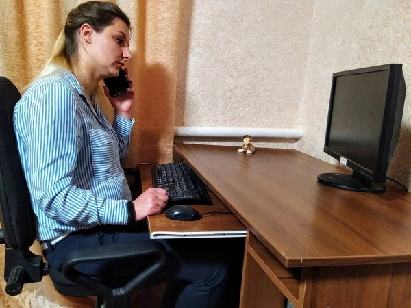 Skoncentrowana Młoda Europejka Siedzi Przy Stole Rozmawia Smartfonie Pracuje Komputerze — Zdjęcie stockowe