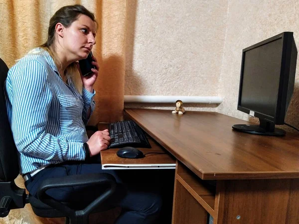 Frightened european young woman sit at table, talk on smartphone and work on computer at home