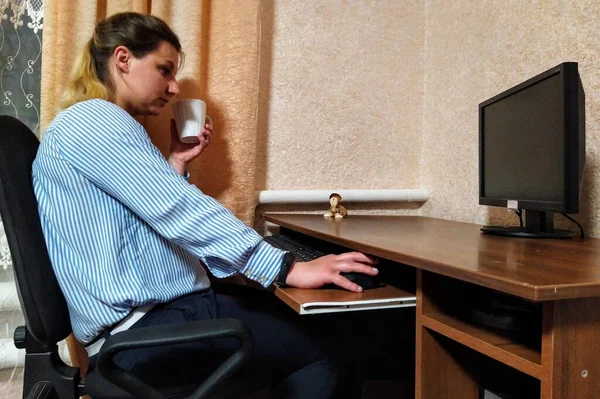 专心致志的欧洲裔年轻女性坐在桌旁 喝茶或喝咖啡 在家里的电脑上工作 — 图库照片