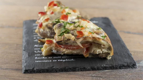 An eggplant appetizer stuffed with vegetables lies on a stone slab.