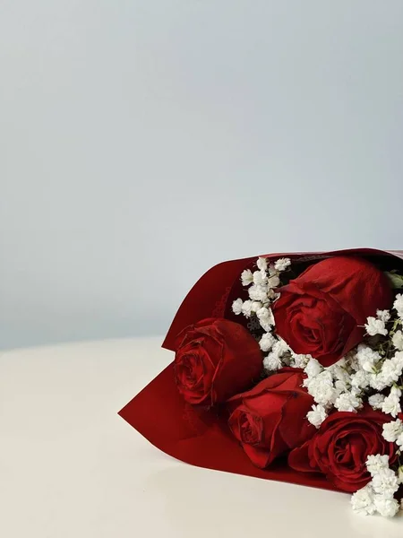 Lovely bouquet of red roses with white wildflowers laying on white table. Minimal concept. Mother's Day, Birthday, Women's Day.