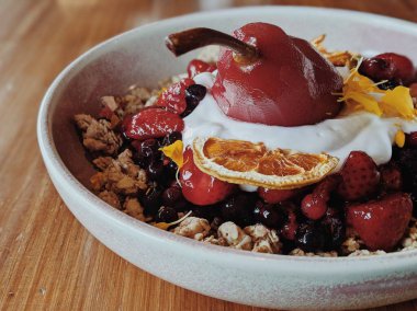 Kahvaltılık granola kasesi, karışık böğürtlen, marine edilmiş armut ve kurutulmuş meyve. Tahta masa. Eşsiz bir tatlı. Sabah sağlıklı yemek.