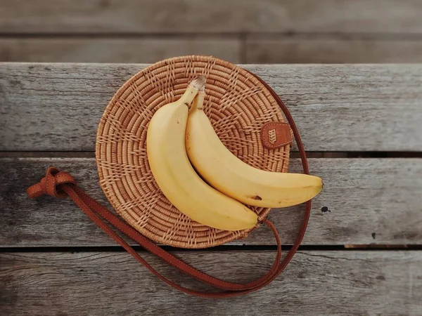 Two bananas on a straw bag laying on a wooden table. Lifestyle. Healthy snack.