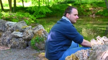 Bir adam iki taş uçlu merdiven arasında gölün kenarında oturuyor.