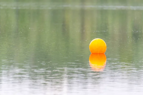 View of a quarry pond with  a special focus on an orange swimming marker from the shore with overcast skies and calm water in northern Germany