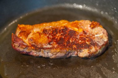 Tavada bifteğin üzerinde yağ olan dilimlenmiş taze bir biftek resmi. Biftek yüksek sıcaklıkta pişiyor.