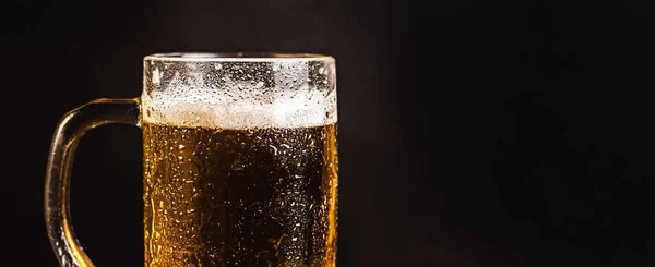 Cold beer with foam in a mug, on a wooden table and a dark background with blank space for a logo or text. Stock Photo mug of cold foamy beer close-up.