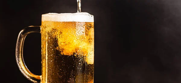 Cold beer with foam in a mug, on a wooden table and a dark background with blank space for a logo or text. Stock Photo mug of cold foamy beer close-up.