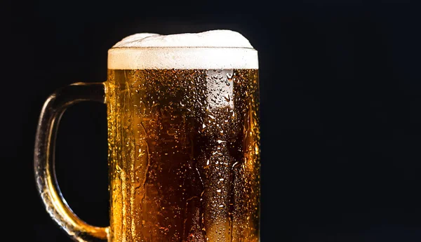 Cold beer with foam in a mug, on a wooden table and a dark background with blank space for a logo or text. Stock Photo mug of cold foamy beer close-up.