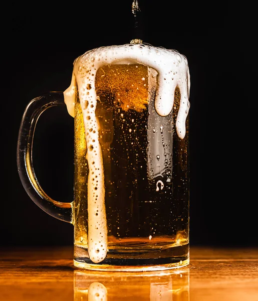 Cold beer with foam in a mug, on a wooden table and a dark background with blank space for a logo or text. Stock Photo mug of cold foamy beer close-up.