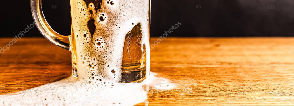 Cold beer with foam in a mug, on a wooden table and a dark background with blank space for a logo or text. Stock Photo mug of cold foamy beer close-up.