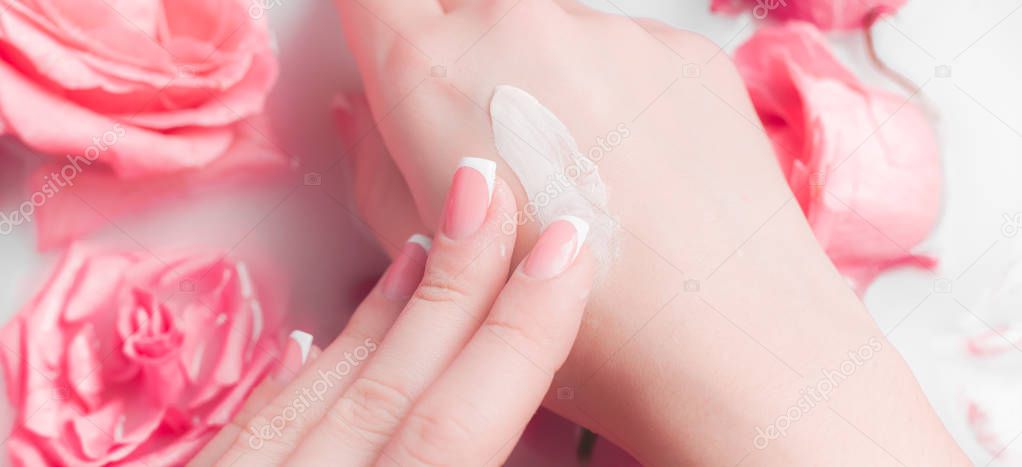 Spa Salon: Beautiful Female Hands with French Manicure in the Bowl of Water with Pink Roses and Rose Petals.