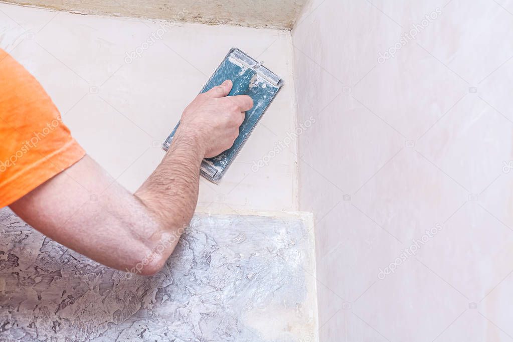 Plasterer smooths the walls with sandpaper close-up. Male hand of a worker. Stock photo.