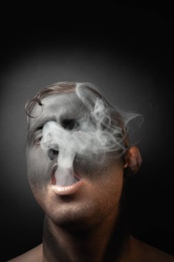 Makyajlı yakışıklı bir adamın yakın plan portresi duman üflüyor. Bir sigara tiryakisinin stok resimleri..