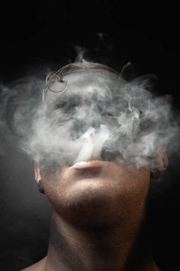 Makyajlı yakışıklı bir adamın yakın plan portresi duman üflüyor. Bir sigara tiryakisinin stok resimleri..