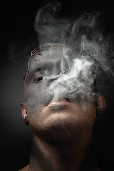 Close-up portrait of a handsome guy in makeup blows smoke. Stock art photo of a smoker.
