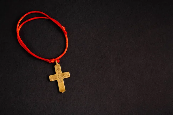 Christian cross on a red rope, on a black background with an empty place. Stock photo cross top.