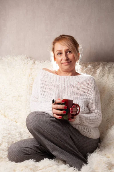 Portrait of an adult woman in a cozy room on the couch with a cup of tea / coffee.