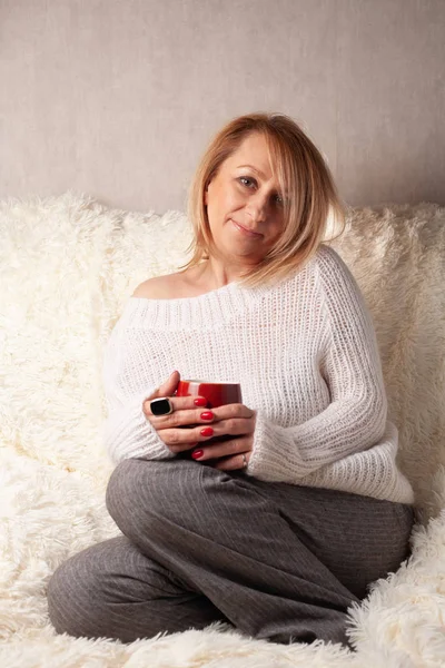 Portrait of an adult woman in a cozy room on the couch with a cup of tea / coffee.