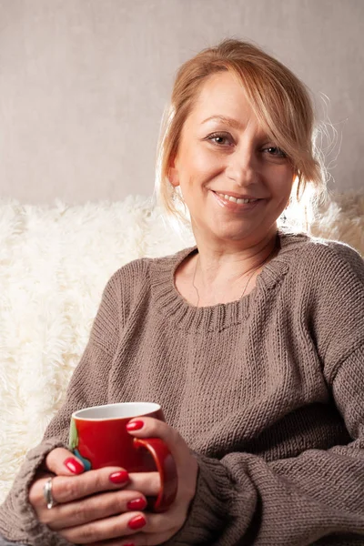 Portrait of an adult woman in a cozy room on the couch with a cup of tea / coffee.