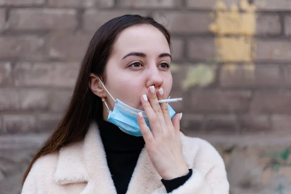 一个戴抗病毒面具的女孩在街上脱下并抽烟 — 图库照片