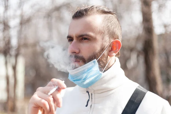 Antiviral maskeli bir adam sokakta sigara içiyor..