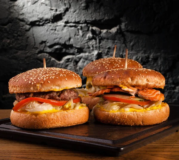 Menu of different burgers on one board. Side view of a fish burger, hamburger and cheese burger, against a wall background.