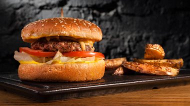 Sehpadaki ahşap masada hamburger ve kırsal patatesler. Siyah bir duvarın arkasında.