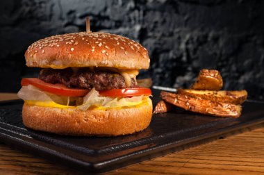 Sehpadaki ahşap masada hamburger ve kırsal patatesler. Siyah bir duvarın arkasında.