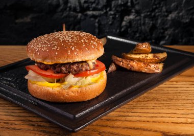 Sehpadaki ahşap masada hamburger ve kırsal patatesler. Siyah bir duvarın arkasında.