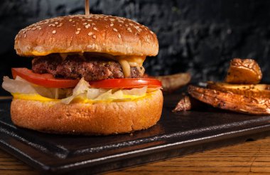 Sehpadaki ahşap masada hamburger ve kırsal patatesler. Siyah bir duvarın arkasında.