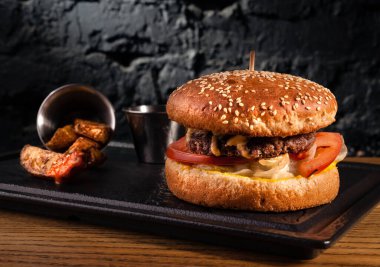 Sehpadaki ahşap masada hamburger ve kırsal patatesler. Siyah bir duvarın arkasında.