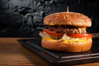 Tahta bir masada iştah açıcı burger ve yan görüş. Güzel desenli siyah bir duvarın arkasında. Boşluk alanı.