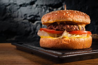 Tahta bir masada iştah açıcı burger ve yan görüş. Güzel desenli siyah bir duvarın arkasında. Boşluk alanı.