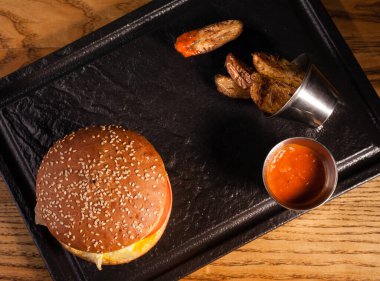 Ahşap bir masa ve siyah bir tepside üst manzara hamburgeri..