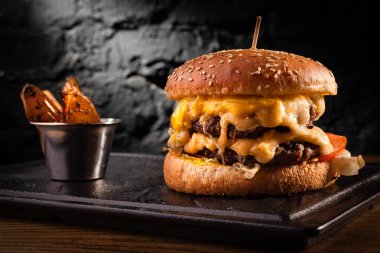 Bol peynirli büyük bir çizburger. Siyah tuğlalı bir duvardaki çizburgerin stok fotoğrafı görünümü.