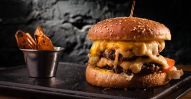 Bol peynirli büyük bir çizburger. Siyah tuğlalı bir duvardaki çizburgerin stok fotoğrafı görünümü.