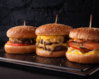 Siyah tuğlalı arka planda arka arkaya çeşitli hamburgerler. Hamburger, çizburger, balık burger..