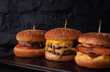 Siyah tuğlalı arka planda arka arkaya çeşitli hamburgerler. Hamburger, çizburger, balık burger..