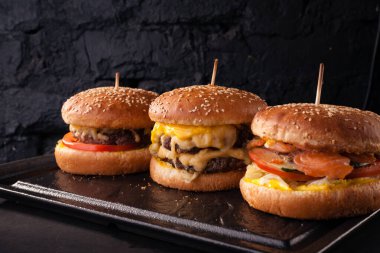 Siyah tuğlalı arka planda arka arkaya çeşitli hamburgerler. Hamburger, çizburger, balık burger..