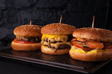 Siyah tuğlalı arka planda arka arkaya çeşitli hamburgerler. Hamburger, çizburger, balık burger..