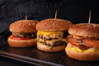 Siyah tuğlalı arka planda arka arkaya çeşitli hamburgerler. Hamburger, çizburger, balık burger..