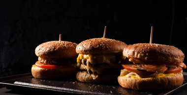 Siyah tuğlalı arka planda arka arkaya çeşitli hamburgerler. Hamburger, çizburger, balık burger..
