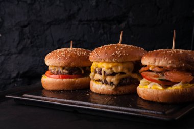 Siyah tuğlalı arka planda arka arkaya çeşitli hamburgerler. Hamburger, çizburger, balık burger..