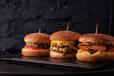 Siyah tuğlalı arka planda arka arkaya çeşitli hamburgerler. Hamburger, çizburger, balık burger..