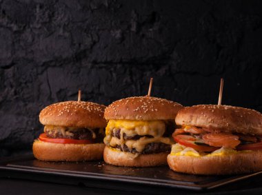 Siyah tuğlalı arka planda arka arkaya çeşitli hamburgerler. Hamburger, çizburger, balık burger..