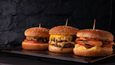 Siyah tuğlalı arka planda arka arkaya çeşitli hamburgerler. Hamburger, çizburger, balık burger..